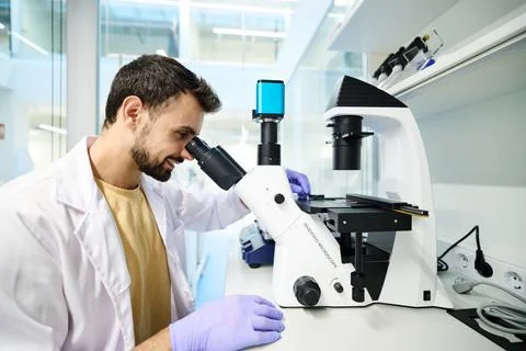 Bearded man examining samples through an inverted microscope in a lab Фото