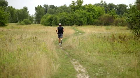 Bearded man exercising with battle rope on grassy trail in summer meadow outside Stock Footage 313951511