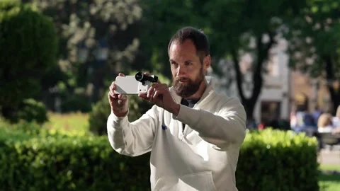 Bearded Man Filming with Smartphone in Horizontal Grip at Subotica Park Stock Footage 334615806