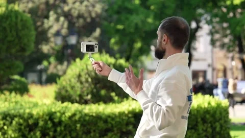 Bearded Man Filming with Smartphone on Three Axis Gimbal Stabilizer in Park Видео 334615805