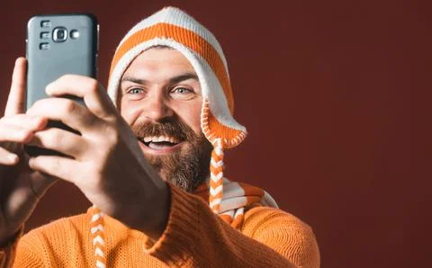 Bearded man in funny hat taking selfie with his smartphone. Photographer ho.. Stock Photos