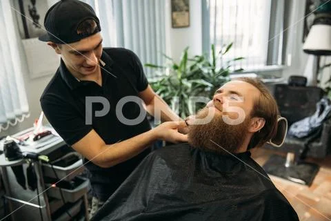 Bearded man getting a haircut by a professional hairdresser using comb and Stock Photos