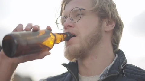 Bearded man with glasses drinking beer and enjoying beverage outdoors. Guy Stock Footage 106458378