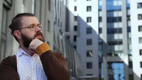A bearded man in glasses looks mindfully to the left and smoothes his beard. Stock Footage 89156014