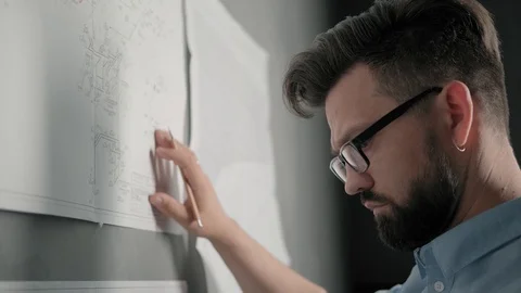 Bearded man with glasses makes notes on blueprints on loft-style wall Stock-Footage 112162120