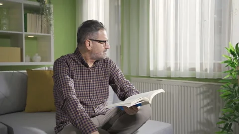 Bearded man with glasses is reading a book by the window. Stock Footage 232208347