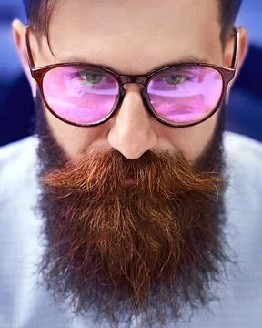 Bearded man in glasses with screen reflection working on computer in IT of... 스톡 사진