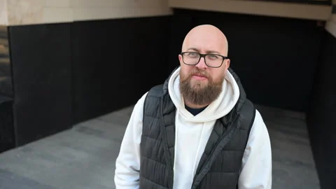 Bearded man in glasses standing confidently in urban alley wearing hoodie and Stock Footage 346742403