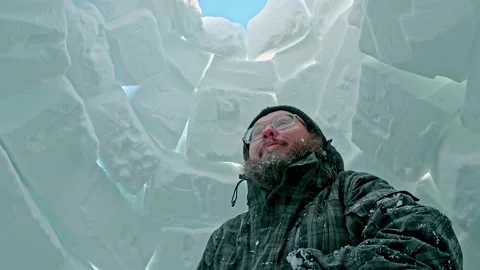 Bearded man in glasses stands inside igloo of white blocks Stock Footage 133828858