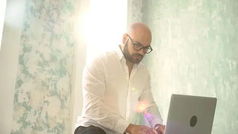 The bearded man with glasses in white using laptop indoors. Businessman working Stock Footage 86682939
