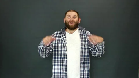 A bearded man on a gray background throws up his hands and says the word Yes Video stock 157859703