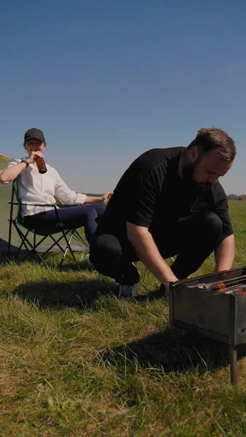Bearded man grilling meat at a sunny outdoor barbecue picnic Stockbeeldmateriaal 344603982
