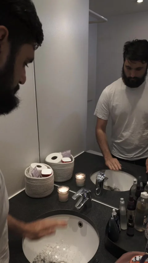 Bearded man grooming beard with electric razor in modern bathroom mirror Video stock 335637264