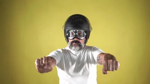 Bearded man with a helmet simulating driving a motorcycle on a yellow backgro Stock Footage 161503495