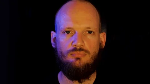 Bearded man in his 30's staring than smiling, blue and yellow side light, Close  Stock Footage 112019829