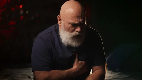 Bearded man in his 50s holds chest in pain at home, heart disease risk Stock Footage 346714344
