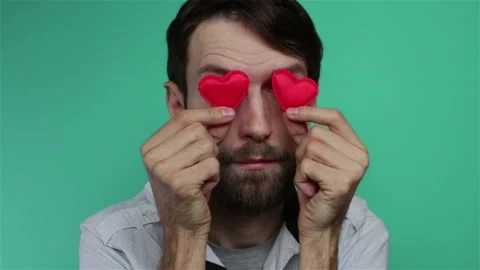 Bearded man holding small red hearts shape near his eyes happy valentines day Stock Footage 120912804