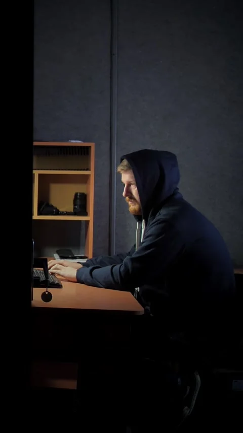 Bearded man in a hood works at a computer by the light of a desk lamp.  Stock Footage 306843484