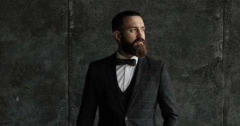 A bearded man ian a suit walk and looks out the window in a contemplative way Stock Footage 79766033