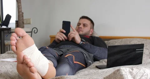 Bearded man with injured leg using his smartphone in the bedroom Stock-Footage 104834603