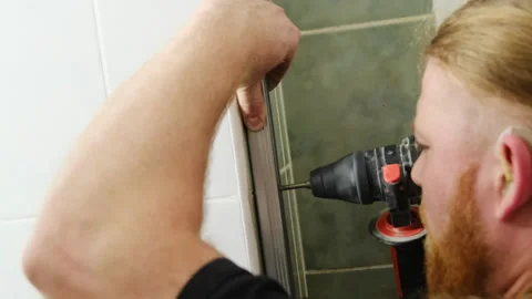 Bearded man installs door system with electric drill in bathroom Video stock 304404486