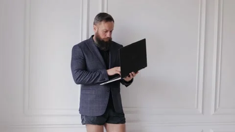 A bearded man in a jacket and without pants works at home in isolation. Stock Footage 131208758