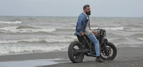 Bearded man in jeans on his old cafe racer motorcycle near sea Stock Footage 140624486