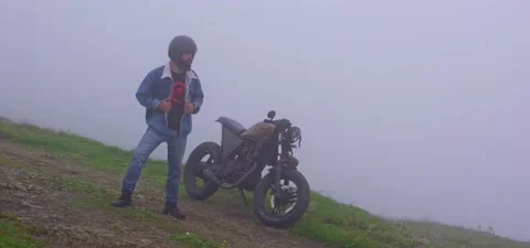 Bearded man in jeans with old cafe racer motorcycle in mountains mist Stock Footage 140623451