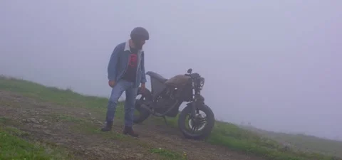 Bearded man in jeans with old cafe racer motorcycle in mountains mist Stock Footage 140623499