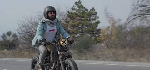 Bearded man in jeans rides old cafe racer motorcycle on country road Stock Footage 140653148