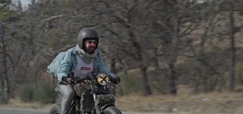 Bearded man in jeans rides old cafe racer motorcycle on country road Stock Footage 140653262