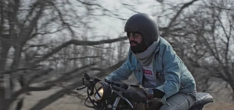 Bearded man in jeans rides old cafe racer motorcycle on country road Stock Footage 140653579