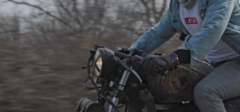 Bearded man in jeans rides old cafe racer motorcycle on country road Stock Footage 140653582