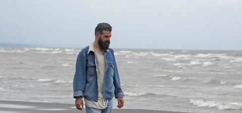 Bearded man in jeans on sandy beach near sea in slow motion Stock Footage 140624565