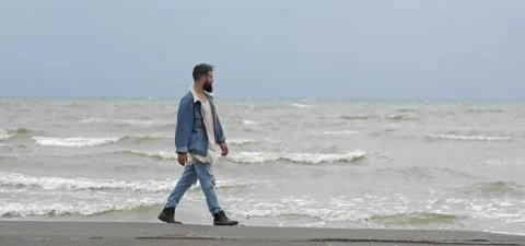 Bearded man in jeans on sandy beach near sea in slow motion Stock Footage 140624614
