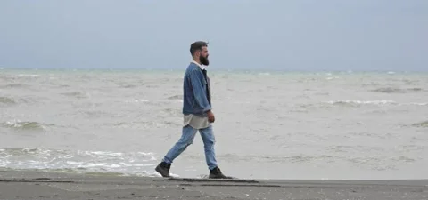 Bearded man in jeans on sandy beach near sea in slow motion Stock Footage 140624651