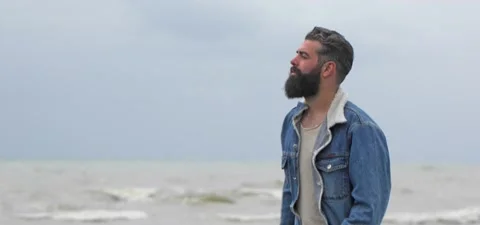 Bearded man in jeans on sandy beach near sea in slow motion Stock Footage 140624705