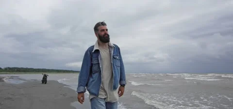Bearded man in jeans on sandy beach near sea in slow motion Video stock 140624710