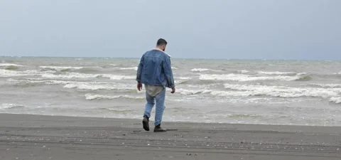 Bearded man in jeans on sandy beach near sea in slow motion Stock Footage 140624752
