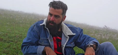 Bearded man in jeans sitting on grass in mountains mist Stock Footage 140623543