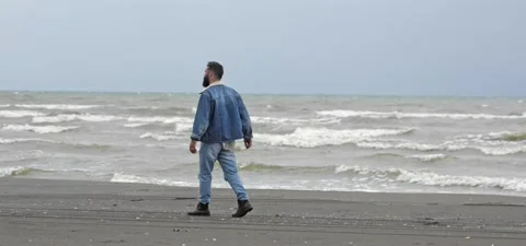 Bearded man in jeans walks on sandy beach near sea in slow motion Stock Footage 140624604