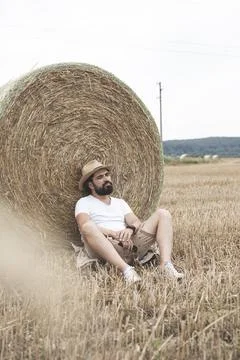 Bearded man leaning on a round bale of dry straw. Stock Photos