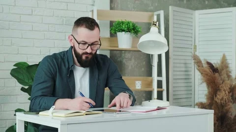 Bearded man learn online courses using a tablet and write notice in his notebook Stock Footage 155640933