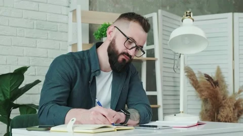 Bearded man learn online courses using a tablet and write notice in his notebook Stock Footage 168976419