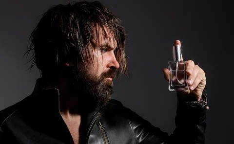 Bearded man in leather jacket with Bottle of perfume or cologne. Cosmetics ad Stock Photos