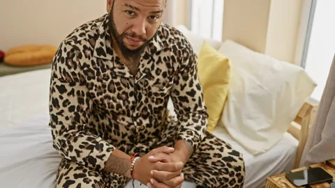 Bearded man in leopard print pajamas sitting thoughtfully on a bed in a coz.. Stock Footage 272194143