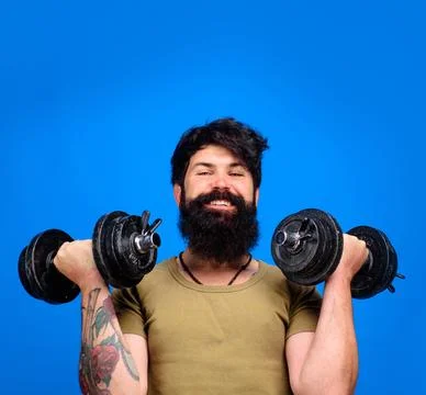 Bearded man lifting dumbbells doing weightlifting. Smiling athlete man with d Stock Photos