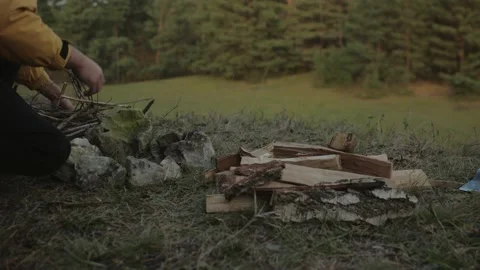A bearded man lights a fire near a makeshift shelter made of pine branches. Stock Footage 220190351