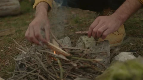 A bearded man lights a fire near a makeshift shelter made of pine branches. Stock Footage 220191611