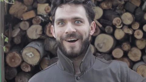 Bearded Man Looking Amazed into the Camera with Wooden Logs in Background Stock Footage 239654550